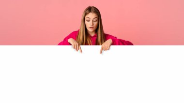 Güzel genç kız pembe arka planda, stüdyo çekimlerinde ve boş alanlarda görünüyor ve gösteriyor.