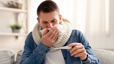 Coronavirus belirtileri. Öksüren adam evde vücut ısısını ölçüyor.