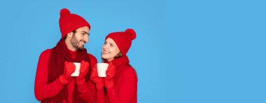 Örgü eldivenler ve şapkalar takan, birlikte kakao içen, sıcak çikolatalı bardakları tutan ve birbirine gülümseyen, mavi arka plan, fotokopi çeken mutlu adam ve kadın.