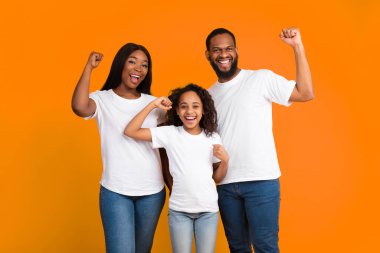 Öyle mi? Heyecanlı genç zenci ailenin portresi yumruklarını sıkarak kazanan jestler yapıyor. Mutlu Afrikalı erkek, kadın ve kız zaferi kutluyor, sarı turuncu stüdyo