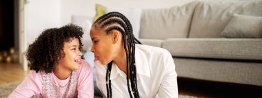 Afrika kökenli Amerikalı anne ve kız, samimi oturma odalarının zemininde oynak ve sevecen bir etkileşime girerek bağlarının sıcaklığını vurguluyorlar..