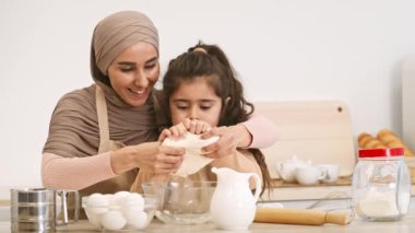 Neşeli bir anne ve kızı mutfakta özel bir anı paylaşıyor, yumurta kırıyor ve pişirmek için malzemeler hazırlıyorlar. Gülüşleri birlikte yemek pişirme sevgisi ve eğlencesini yansıtıyor..