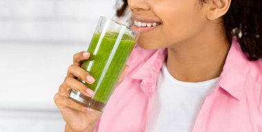 Detox konsepti. Elinde ev yapımı yeşil meyve suyu olan, boş alana bakan siyah bir kızın portresi.