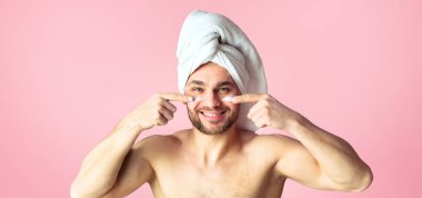 Erkek vücut bakımı kavramı. Duştan sonra tatlı bir genç adam, kafasında beyaz havlu, yüzüne krem sürmüş..