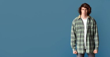 Milenyum adamı öfkeyle yumruklarını sallıyor ve turkuaz arka planda kaşlarını çatıyor.