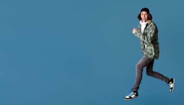 Kulaklıklı, turkuaz arka planda zıplayan komik milenyum adamı, boşluğu kopyala