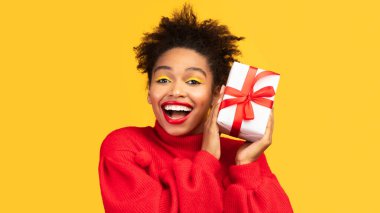 Doğum günün kutlu olsun. Elinde hediye kutusu olan mutlu afro kızın portresi, kameraya, telif alanına, sarı stüdyo duvarına bakıyor.