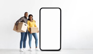 Neşeli siyah bir çift bir arada duruyor, ellerinde karton kutular. Büyük boş bir telefon çerçevesinin yanında konumlanmışlar, neşeli bir atmosfer yaratıyorlar. Gülüşleri heyecan ve takım çalışmasını yansıtıyor..
