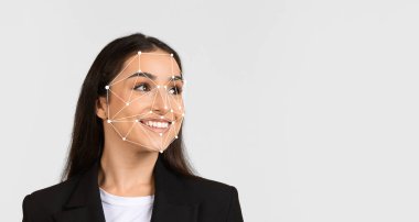 Yüzünde yüz tanıma işaretleri belirdiğinde bir kadın gülümseyerek hafifçe yana bakıyor. Arka plan sade, insan ifadelerindeki teknolojiye odaklanmayı vurguluyor..