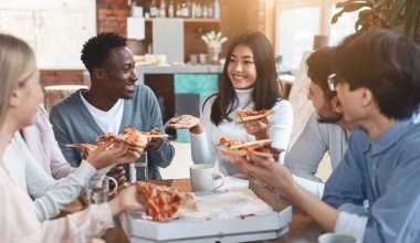 Cheerful international colleagues eating take away food in office during lunch break