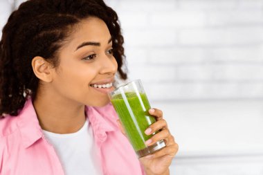Detox konsepti. Elinde ev yapımı yeşil meyve suyu olan, boş alana bakan siyah bir kızın portresi.