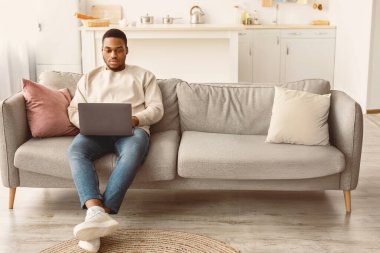 Aile Gadget 'ları. Kanepede aletleriyle oturan Afrikalı Amerikalı çift, dijital tablet kullanan kadın, dizüstü bilgisayar tutan erkek, evde interneti birlikte gezen kadın. Modern Yaşam Tarzı Konsepti, Uzayı Kopyala