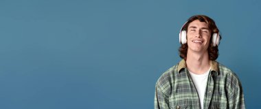 Kulaklık takmış havalı bir gencin portresi turkuaz arka planda en sevdiği müzikle dinleniyor.