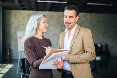 A woman and a man engage in a lively discussion in a contemporary office, with the woman taking notes on a notepad. Their expressions reflect collaboration and creativity. clipart