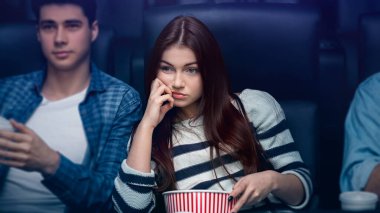 Sıkıcı randevu konsepti. Erkek arkadaşı olan yorgun genç bir kız karanlık sinemada film izliyor.