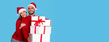 Mutlu genç çift, Noel hediyelerini sunuyor ve kameraya gülümsüyor, Noel Baba Şapkalı neşeli adam ve kadın birlikte kış tatillerini kutluyor,