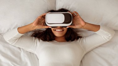 VR kulaklık takan, Sanal Gerçekliği Deneyen, Yatakta Uzanmış Gerçekliği Keşfeden, gülümseyen Afrikalı Amerikalı Kadın. Üst Görünümün Üzerinde, Panorama, Banner, Beleş Kopyalama Boşluğu