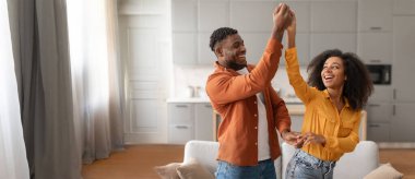 African American couple enjoys a moment of happiness as they dance together in a stylish living room. The warm atmosphere enhances their joyful expressions and lively interaction. clipart