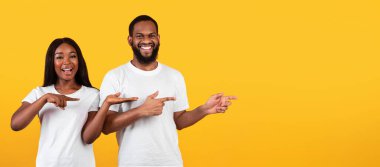 Şuna bak. Sarı arka planda iki parmağıyla işaret eden olumlu siyahi çiftin portresi reklamınız, panoramanız ve pankartınız için bedava yer gösteriyor.