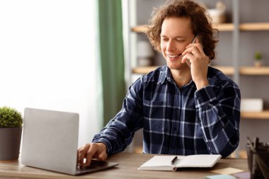 Neşeli Milenyum İşadamı cep telefonuyla konuşuyor. Modern Ofiste İşyerinde Dizüstü bilgisayarda çalışıyor. Serbest Çalışan Adam içeride telefonla konuşuyor. Mobil İletişim. Yan Görünüm