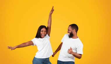 Eğleniyorum. Heyecanlı genç siyahi çiftin dans edip oynaşmaları. Duygusal olarak mutlu olan Afrikalı erkek ve kadın sarı stüdyo arka planında favori müziğin tadını çıkarıyorlar.