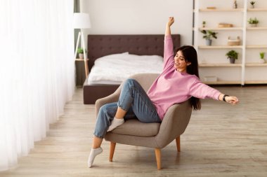 Tam rahatlama ve memnuniyet kavramı. Rahat bir sandalyede oturan, kollarını kaldıran ve hafta sonu oturma odasında dinlenen güzel bir kadının portresi. İyilik, refah.