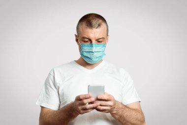 Sosyal Mesafe. Maskeli Adam internetten yemek sipariş ediyor. Karantina sırasında evde kalıyor. Gri Arkaplan, Seçici Odaklanma