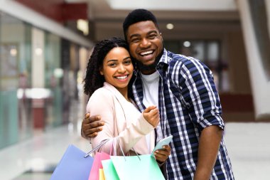 Başarılı bir alışveriş sonrası alışveriş merkezinde poz veren neşeli siyah eşler, modern mağazada alışveriş yapmaktan keyif alan, mutlu Afrikalı Amerikalı erkek ve kadınlar kameraya sarılıp gülümsüyor,