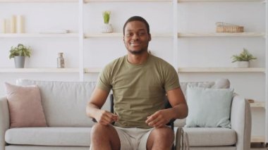 Yeşil tişörtlü ve beyaz şortlu Afro-Amerikalı bir adam oturma odasında tekerlekli sandalyede oturuyor. O, kameraya gülümsüyor. Arkasında iki yastıklı beyaz bir kanepe var..