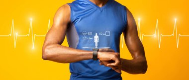 Uygun bir kavram. Siyah kaslı adam fitness izleyicisini kontrol ediyor, sarı stüdyo duvarı, panorama, arka planda kalp atışı çizgisi