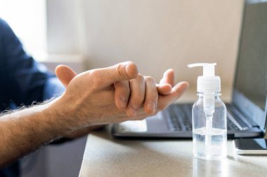 Evde dizüstü bilgisayarda çalışan tanınmayan adam tıbbi dezenfektan jel sterilize ediyor. Kırpılmış, Panorama, Seçici Odaklanma