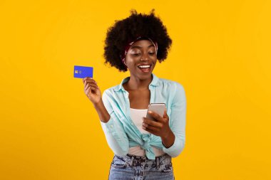 Mobil Alışveriş Uygulaması. Smartphone Holding Credit Card 'ı kullanan mutlu Afrikalı kadın çevrimiçi alışveriş uygulamasında kıyafet satın alıyor. Stüdyo Çekimi