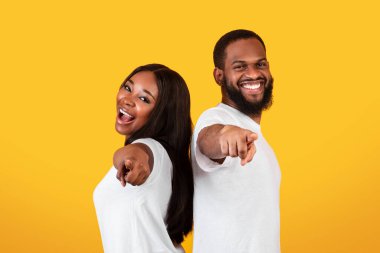 Senin sıran. Heyecanlı Afrikalı Amerikalı genç bir çiftin portresi, kamerayı işaret eden mutlu adam ve kadının seni seçmesi, arka arkaya izole edilmiş sarı stüdyo arka planı, kopyalama alanı.