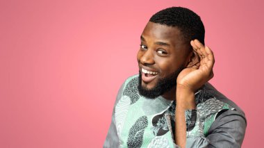 Curious interested african-american man holding hand near ear and trying to hear information, pink studio background, copy space. Excited black guy in traditional costume eavesdropping clipart