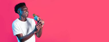 Beyaz tişörtlü genç bir zenci mikrofona tutkuyla şarkı söylüyor, parlak bir şekilde gülümsüyor. Canlı pembe arka plan onun enerjik performansına canlı bir dokunuş katıyor..