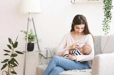 Emzirme konsepti. Genç anne bebeğini evdeki kanepede emziriyor.