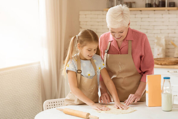 Счастливая семья на кухне. Зрелая женщина и ее внук делают тесто для выпечки в помещении
