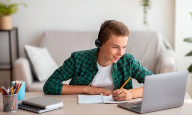 Not defterine yazan neşeli genç adam ve dizüstü bilgisayara bakan, çevrimiçi ders alan, ev içi, serbest alan