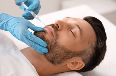 Çekici sakallı adam estetik kliniğe gidip dudak dolgusu yaptırıyor, yakın plan çekiyor. Orta yaşlı iş adamı erkek spa salonunda güzellik iğnesi yaptırıyor. Yüz bakımı, erkek konsepti için yaşlanma karşıtı tedavi