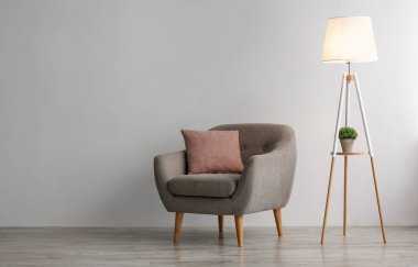Pembe yastıklı rahat bir koltuk. Ofiste ya da oturma odasında gri duvarda parlayan bir lamba. İskandinav tarzı, minimalist, modern ev içi, gayrimenkul reklamı ve modern blog