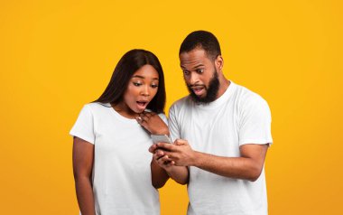 Şok Olan Siyah Adam 'ın Cep Telefonu Tutuşu ve Şaşırmış Kadın' a Açık Ağzıyla Ekran Gösterme, Medya Paylaşımı. Duygusal Çift Cep Telefonu, Orange Stüdyo Arkaplanı, Banner