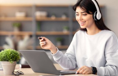 İnsanlar ve Modern Teknoloji Konsepti. Kablosuz kulaklık takmış gülümseyen bir kadının portresi, dizüstü bilgisayar kullanıyor ve deftere yazıyor, not alıyor, ders izliyor ya da çalışıyor, kalem tutuyor.