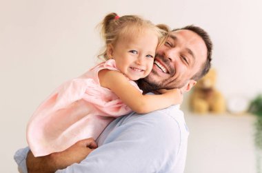 Sevgi dolu bir aile. Baba küçük kızına sarılıyor ve kameraya bakıyor. Uzayı kopyala, afiş