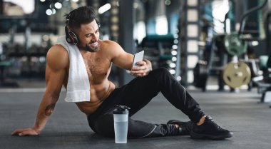 Cep telefonu online kişisel eğitmen. Spor salonunda cep telefonu kullanan kaslı adam, boş alan