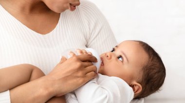 Bebekler için beslenme. Afrika kökenli Amerikalı anne, bebeğini süt şişesiyle besliyor. Küçük sevimli oğluna evde süt veriyor. Çocuk Bakımı, Bebekler İçin Gıda Reklamı Konsepti. Kırpılmış