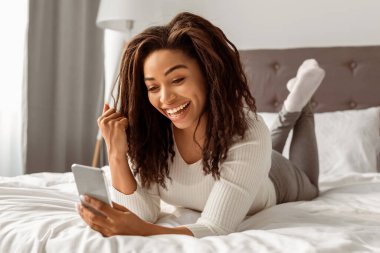 Büyük Galibiyet. Neşeli Afro-Amerikan Kadın Zeka Telefonu Tutan Neşeli ve Heyecanlı Yumruğun Portresi. Evde yatakta yatan genç ve mutlu bir bayan. Evet, harika haber ve mesaj konsepti.