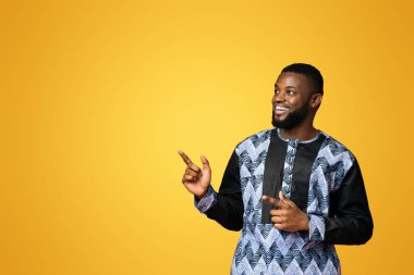 Geleneksel kostümlü neşeli siyah adam reklam, pembe arka plan, panorama için boş yeri işaret ediyor. Renkli tişörtlü Afro-Amerikan 'ın stüdyo fotoğrafı boş yer gösteriyor.