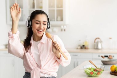 Eğleniyorum. Kulaklık takan, müzik dinleyen, dans eden, tahta spatulayı mikrofon olarak kullanan, mutfakta dikilen, bedava fotokopi alanı olan neşeli gülümseyen bin yıllık kadının portresi.