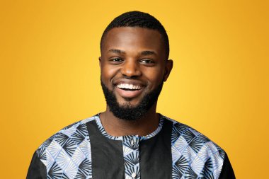 Geleneksel Afrika kostümü giyen gülümseyen zenci adam portresi, pembe stüdyo arka planı, boş alan. Mutlu Afro-Amerikalı adam renkli siyah ve gri ulusal kıyafetler gösteriyor.