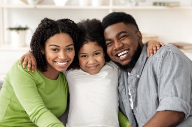 Mutlu Afro-Amerikan aile pozu, evde portre çekimi, kucaklama ve kameraya gülümseme,